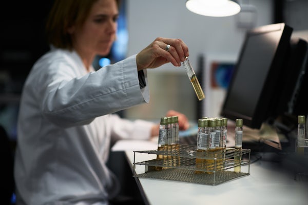 A technician wearing a white lab coat analyzes test tubes.